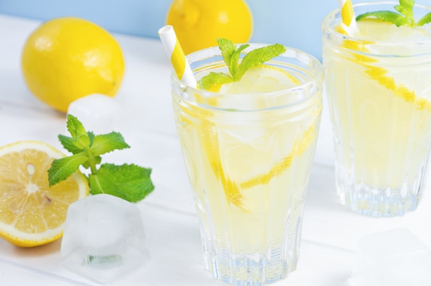 Gläser mit Sommergetränklimonade, Zitronenfrucht und tadellosen Blättern auf weißem Holztisch.