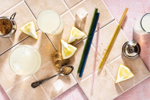 Gläser mit Sommerlimonade und Rohrzucker auf rosafarbenem Hintergrund Glasstrohhalme für Getränke