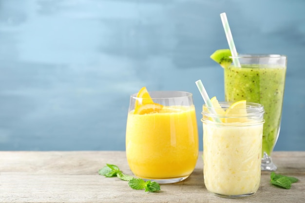 Gläser mit verschiedenen Smoothies auf dem Tisch vor farbigem Hintergrund