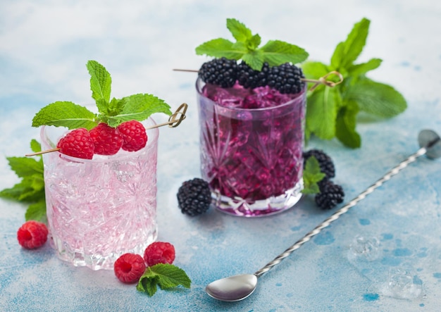 Gläser rosa Limonade und Brombeercocktail mit Eiswürfeln und Minze auf blauem Hintergrund mit Barlöffel