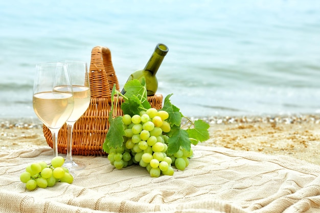 Gläser Wein und Korb mit Flasche und frischen Trauben am Strand