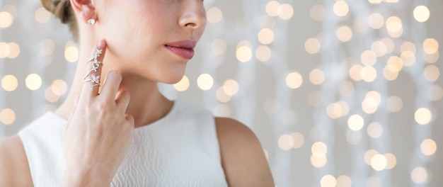 glamour, beleza, joias e conceito de luxo - close-up de mulher bonita com anel de ouro e brinco de diamante sobre fundo de luzes de férias