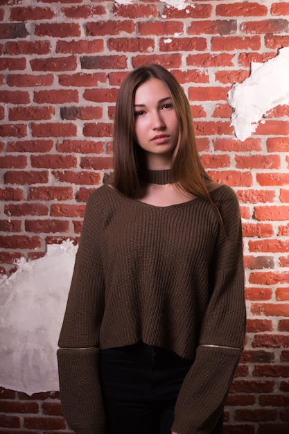 Glamour-Brünette-Modell mit langen Haaren posiert auf einem Backsteinmauer-Hintergrund