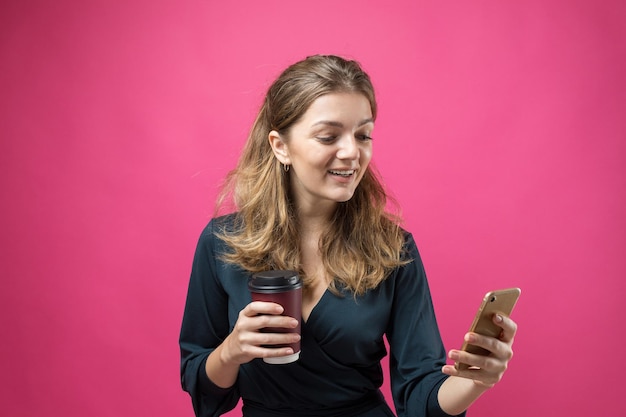 Glamour-Frau in einem dunkelblauen Kleid mit einem Schluck Kaffee auf rosa Hintergrund