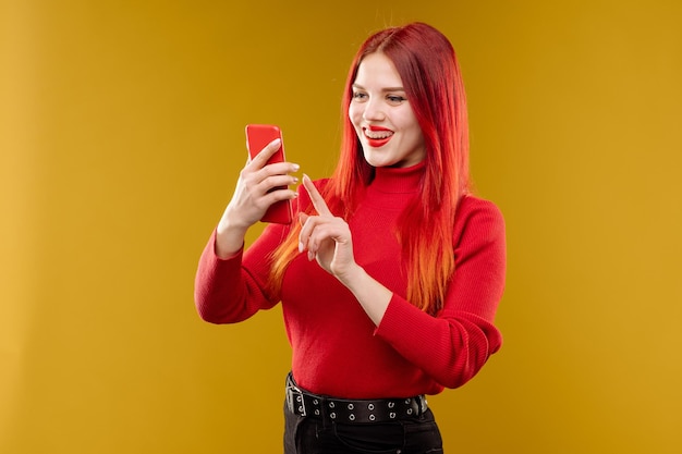 Glamour-Frau mit roten Haaren mit Smartphone auf gelbem Hintergrund