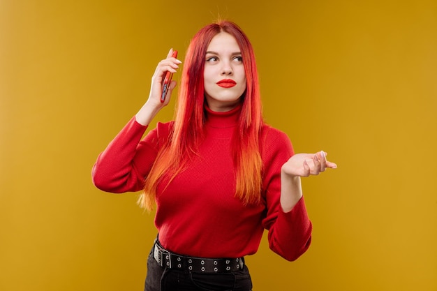 Glamour-Frau mit roten Haaren mit Smartphone auf gelbem Hintergrund