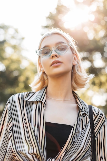 Glamour jovem mulher bonita com cabelo loiro shorts em roupas de verão com óculos de sol azuis caminha ao ar livre