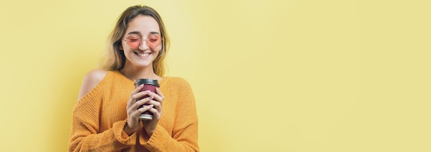 Glamour mulher de óculos em um suéter laranja com uma bebida de café em um fundo amarelo