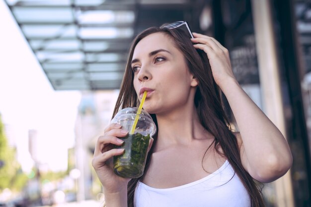 Glamour-Trend, stilvolles urbanes Leben, Spaziergang, Rush-Bewegung, Kaufzentrum, Innenstadt, Konzept. Nahaufnahme Porträt ziemlich schöne nachdenkliche nachdenkliche Studentenperson, die frische Schrägstrichtasse in der Hand weißes T-Shirt hält