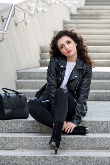 Glamouröse junge brünette Frau in der schwarzen Lederjacke, die auf der Stadtstraße aufwirft und Spaß hat