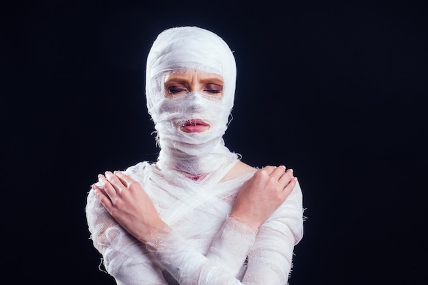 Glamouröse Mumienfrau in Verbänden am ganzen Körper im schwarzen Hintergrund des Studios. Halloween-Party oder Opferkonzept für plastische Chirurgie.