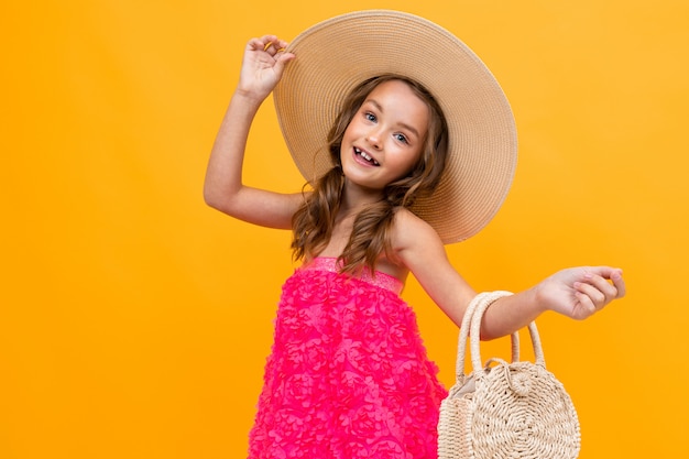 Glamouröser junger Fashionista mit Strohhut und runder Tasche an gelber Wand