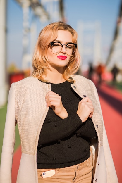 Glamouröses blondes Model trägt eine klare Brille mit hellem Make-up und posiert im Sonnenlicht