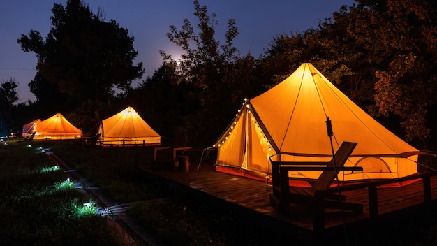 Glamping à noite, poucas tendas brilhantes, luzes noturnas