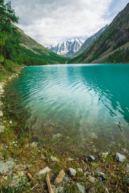 Glanzwasser im Gebirgssee im Hochland. Wunderbare riesige schneebedeckte Berge. Creek fließt vom Gletscher. Weißer klarer Schnee auf Kamm. Erstaunliche atmosphärische Landschaft der majestätischen Altai-Natur.