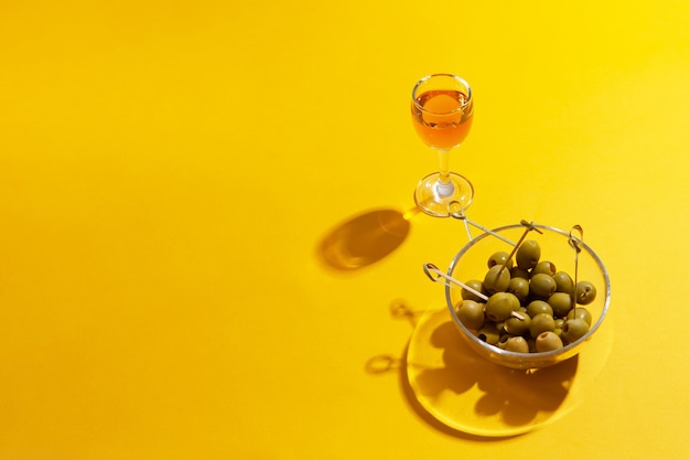 Foto glas alkohol mit grünen oliven in glasschüssel auf gelb mit kopierraum