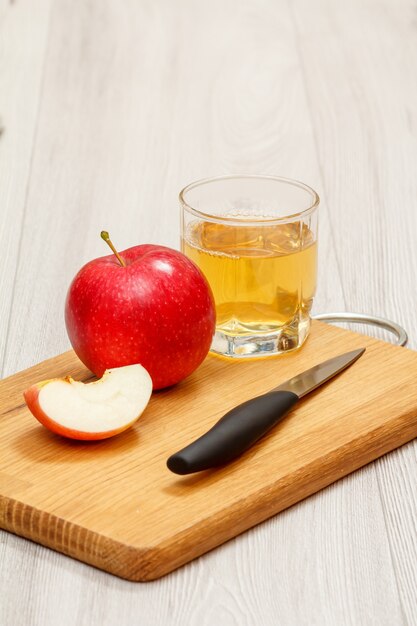 Glas Apfelsaft mit rotem Apfel, in Scheiben geschnitten und Messer auf Holzbrett.