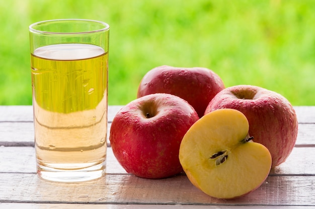 Glas Apfelsaft und rote Äpfel auf Holztisch mit natürlichem grünem Hintergrund