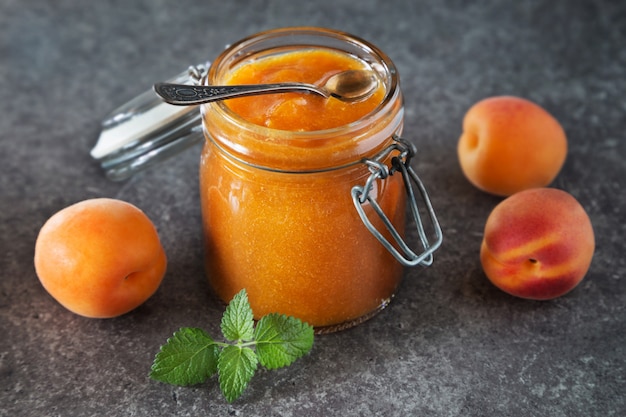 Glas aprikosenmarmelade mit löffel auf grauer tabelle