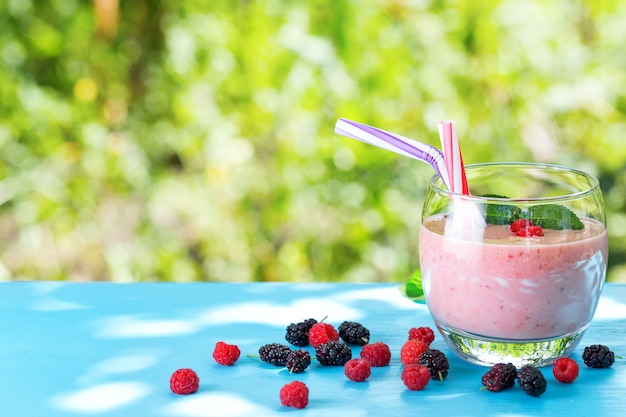 Glas Beeren-Smoothie mit Stroh und Beeren auf blauem Tisch