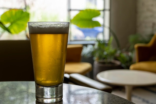 Glas Bier auf einem Terrazzo-Tisch Zwei gelbe Stühle im Hintergrund Retro-Tischfenster mit natürlichem Licht