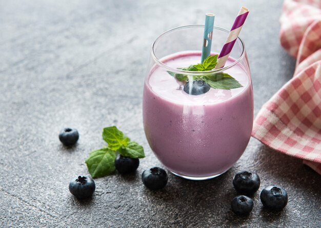 Glas Blaubeerjoghurt mit Blaubeeren auf grauem Steinhintergrund.