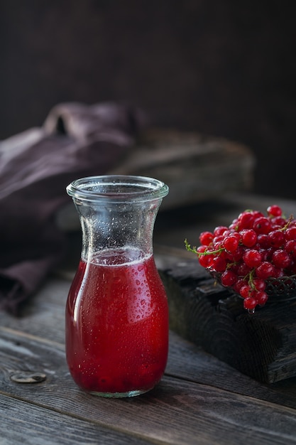 Glas Cocktail mit roten Johannisbeeren oder Cocktail, erfrischendes Sommergetränk mit Crushed Ice und Mineralwasser auf dunklem Holz