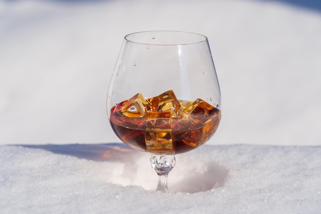 Glas Cognac mit Eis auf einem Bett aus Schnee und weißem Hintergrund hautnah