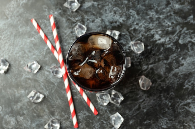 Glas Cola, Eis und Strohhalme auf schwarzem, rauchigem Hintergrund.