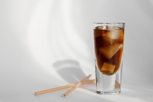 Glas cola mit eis und stroh auf einer weißen wand