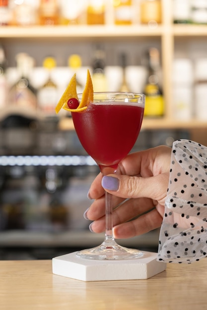 Glas Cranberry-Cocktail und weibliche Hand auf Bar-Hintergrund