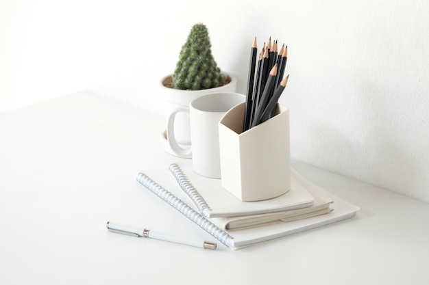 Glas des Bleistifts und des Bürozubehörs mit Kaktus auf weißer Tabelle.