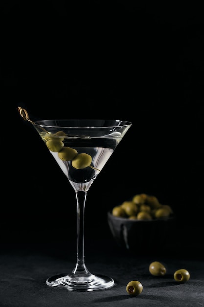 Glas des klassischen trockenen Martini-Cocktails mit Oliven auf dunklem Steintisch gegen Schwarz