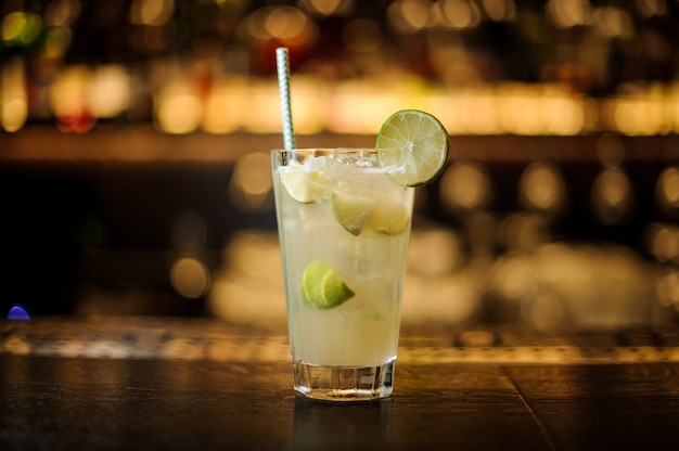 Glas eines Limonadencocktails mit Limetten- und Eiswürfeln auf der Bartheke aus Holz