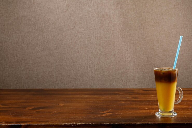 Glas Eiskaffee mit Orangensaft auf Holztisch über leerer Wand. Platz kopieren