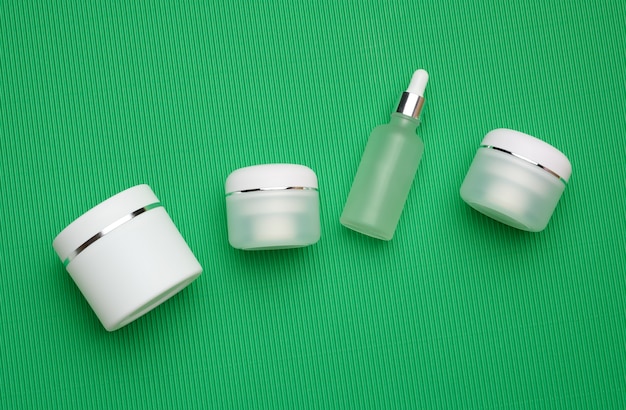 Glas, Flasche und leere weiße Plastikröhrchen für Kosmetika auf grünem Hintergrund. Verpackungen für Creme, Gel, Serum, Werbung und Produktwerbung, Mock-up