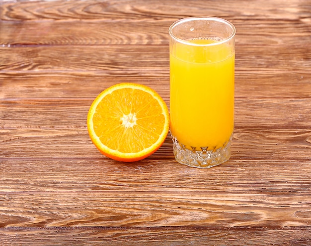 Glas frisch gepresster Orangensaft mit geschnittener Orangenhälfte auf Holztisch