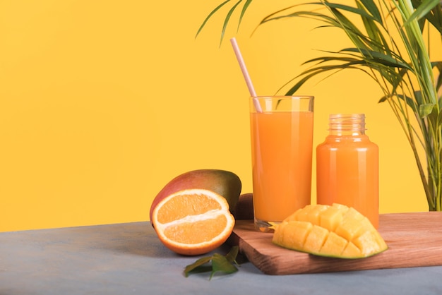 Glas frischen Orangen- und Mangosaft und Scheibe Orangenfrucht auf gelbem Hintergrund