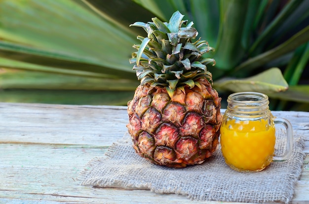 Glas frischer Ananassaft und reife Ananasfrucht auf rustikalem Holztisch. Frisch gepresster Ananassaft mit Trinkhalm. Gesundes Essen, Diät oder veganes Lebensmittelkonzept.