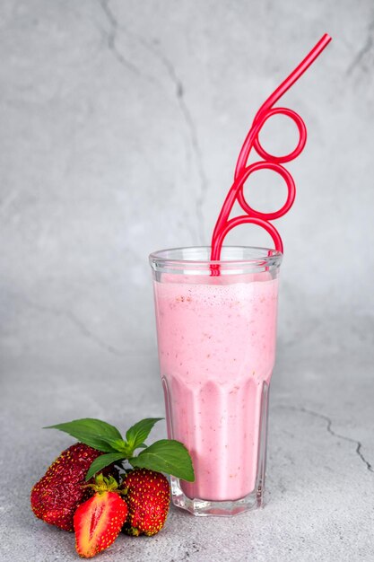 Glas frischer Erdbeer-Milchshake-Smoothie und frische Erdbeeren auf grauem Hintergrund Konzept für gesundes Essen und Trinken