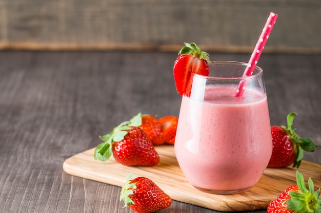 Glas frischer Erdbeermilchshake, Smoothie und frische Erdbeeren auf rosa, weißem und hölzernem Hintergrund. Gesundes Essen und Trinken Konzept.