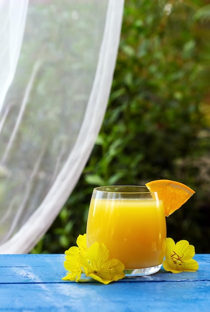 Glas frischer Orangensaft, garniert mit einer Scheibe reifer Orange und Blumen auf dem blauen Holztisch