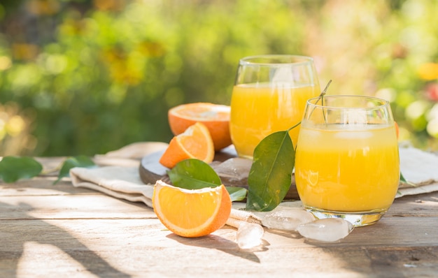 Glas frischer Orangensaft, reife Orangenfrüchte und Scheiben auf natürlichem. Frisch gepresster Orangensaft mit Trinkhalm, Orangenfrüchten und Orangenscheiben.