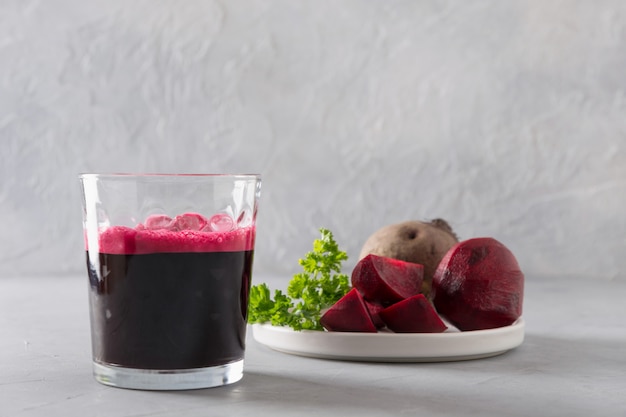 Glas frischer Rote-Bete-Wurzeln Saft schmücken Petersilie auf Grau.