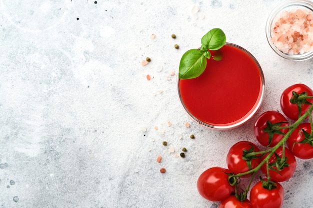 Glas frischer Tomatensaft, Salz, Basilikum und Tomaten auf altem hellgrauem Hintergrund. Draufsicht mit Kopienraum.