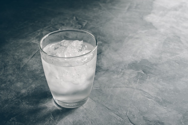 Glas frisches Mineralwasser mit Eiswürfeln auf Zementtabelle mit Weinlesefarbe. Leere bereit für Ihre Produktanzeige oder Montage.