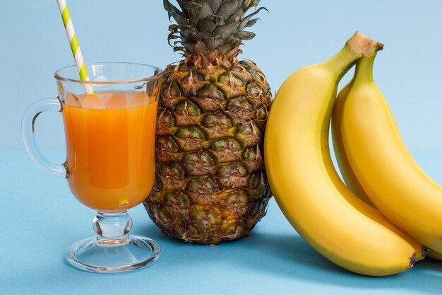 Glas Fruchtsaft, frische Ananas und Bananen auf blauem Hintergrund.