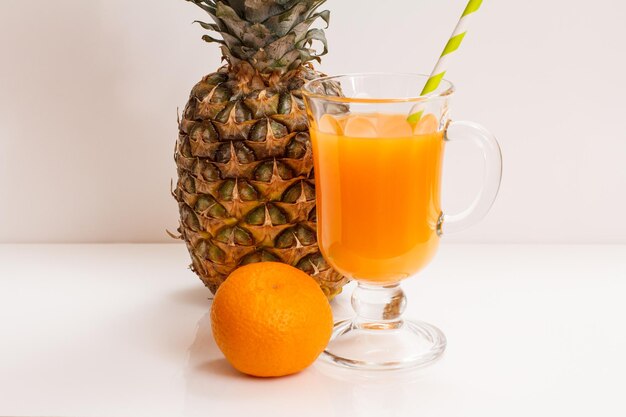 Glas Fruchtsaft mit Strohhalm, frischer Ananas und Mandarine auf weißem Hintergrund.