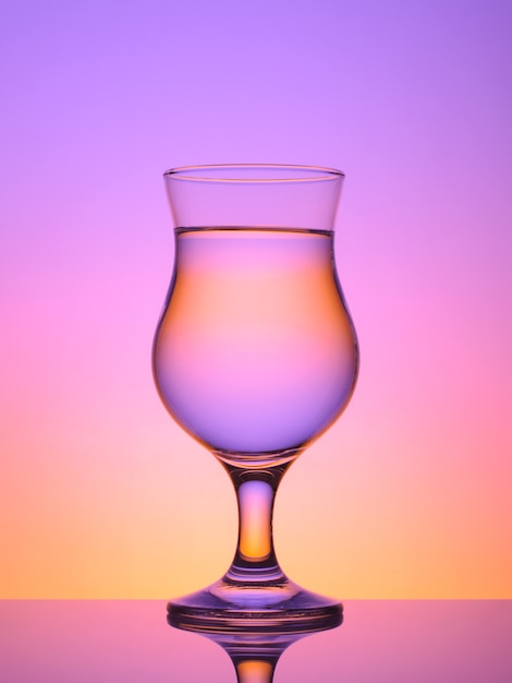 Foto glas für cocktail mit wasser auf farbigem hintergrund, mit reflexion, sonnenuntergangsfarbe, lila; rosa; orange;