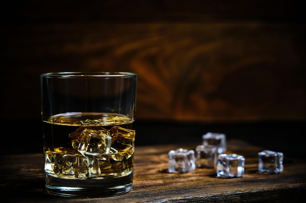 Glas gekühlter Whisky mit Eiswürfeln auf Holzhintergrund im Keller.